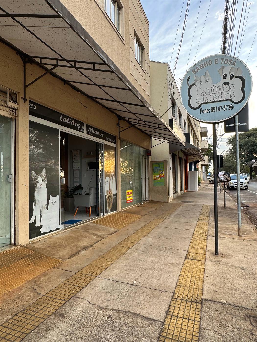 Fachada da Latidos e Miados vista da calçada, com a placa de banho e tosa